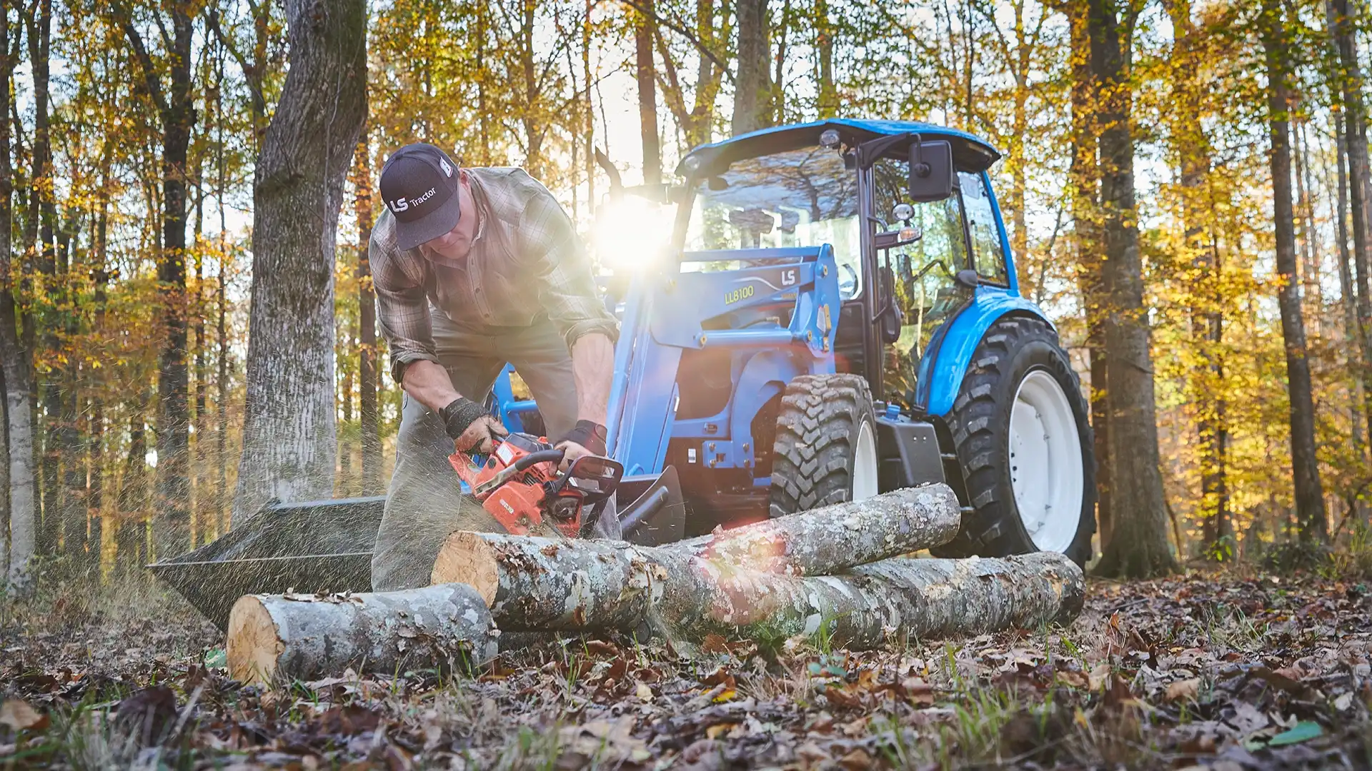 a man cuts wood with a chainsaw in front of an ls tractor